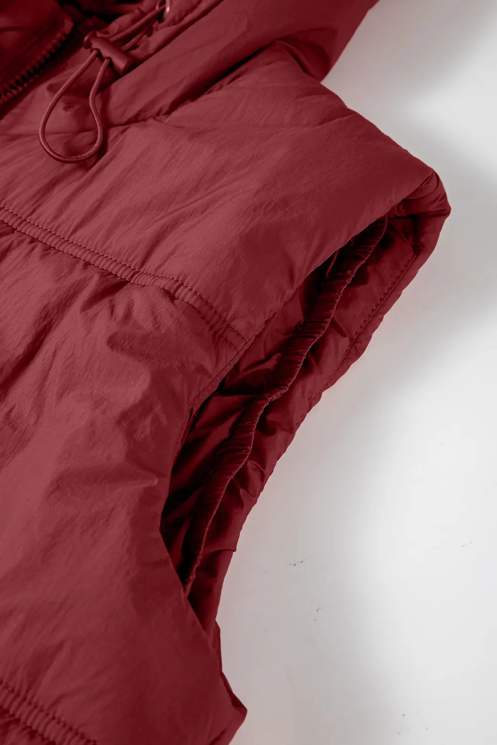 Close-up of burgundy hooded puffer vest coat sleeve/side seam and zipper trim