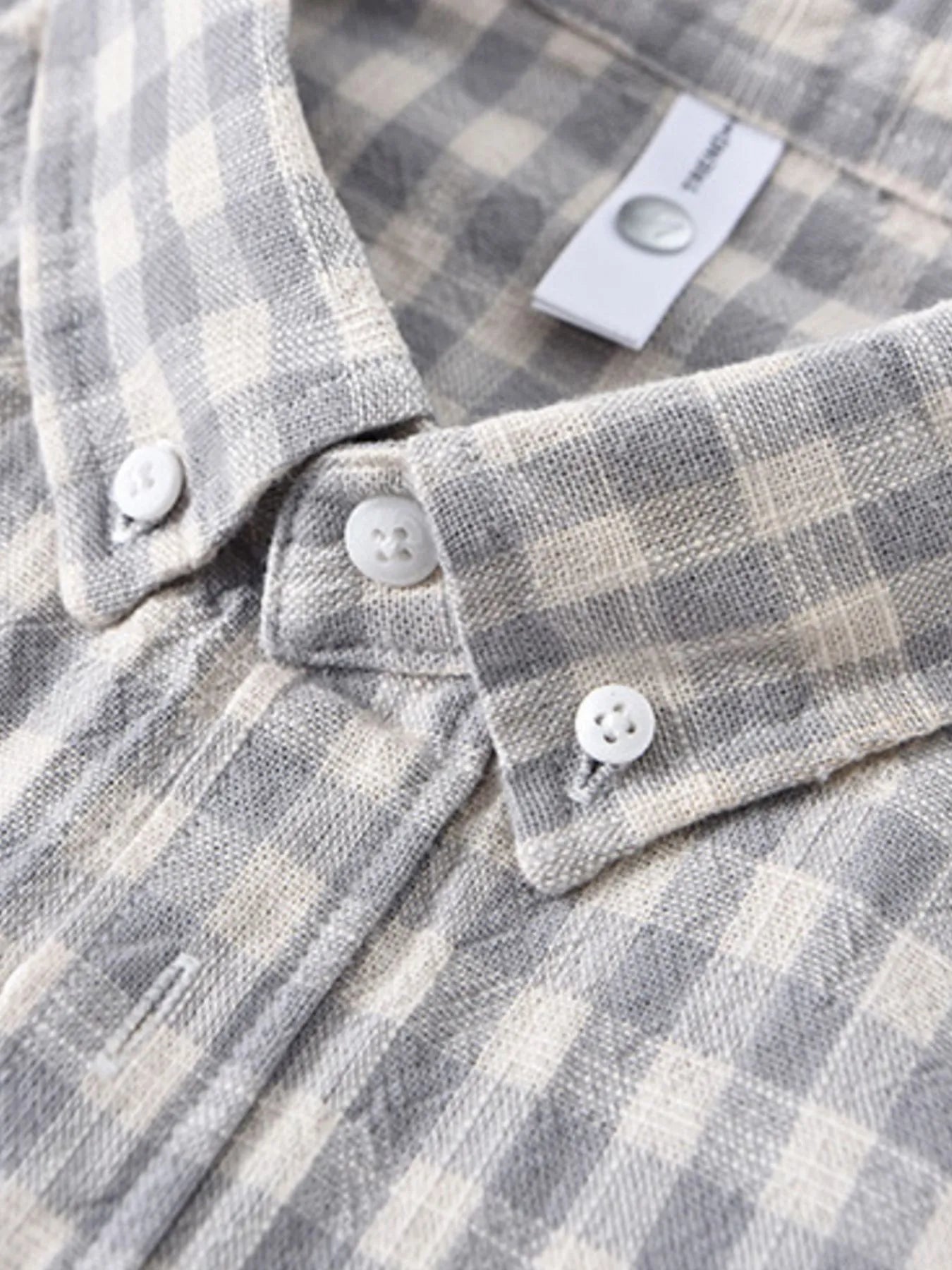 Gray plaid button-up shirt cuff close-up with white buttons and stitched placket