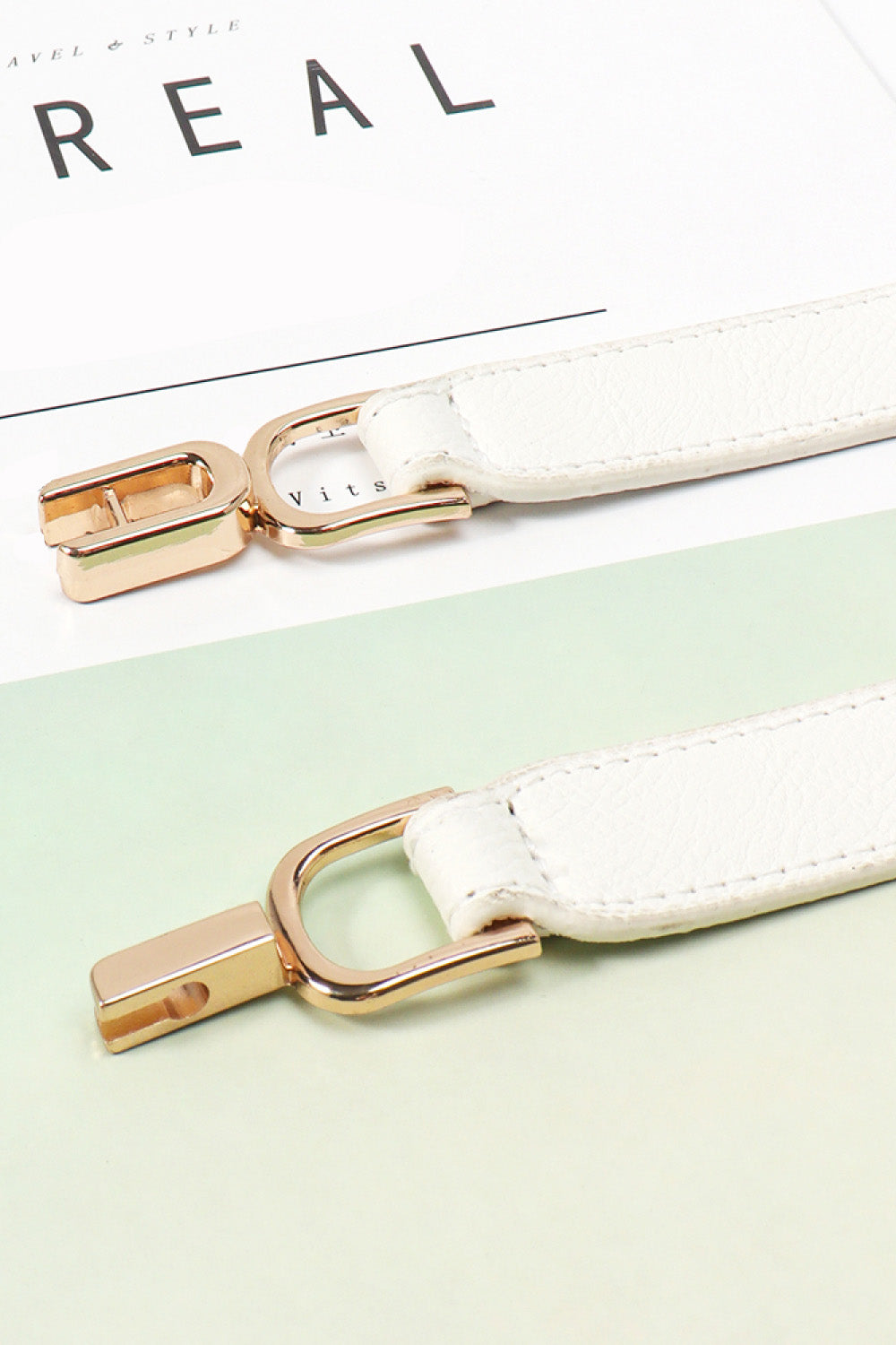 White elastic belt close-up with gold-tone buckle clips and silver-tone ring detail