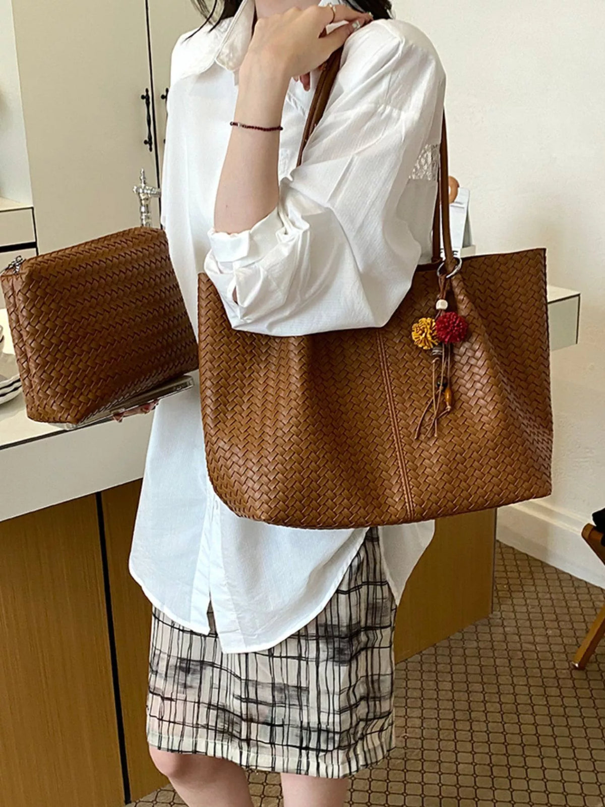 Brown woven vegan leather tote bag with long handles, zipper top, and tassel charm