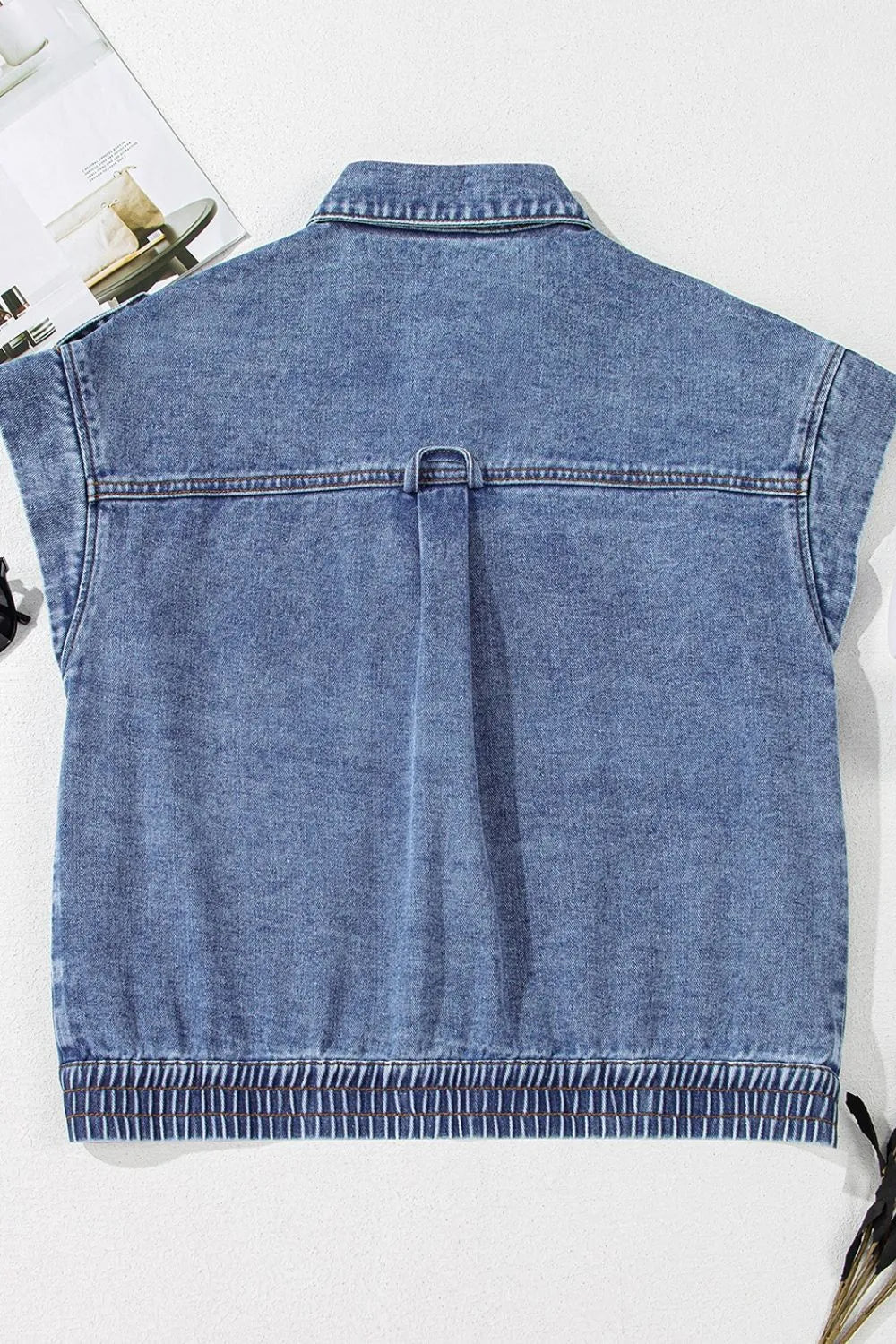 Medium-wash denim button-up cap sleeve jacket on flat lay, back view with center seam