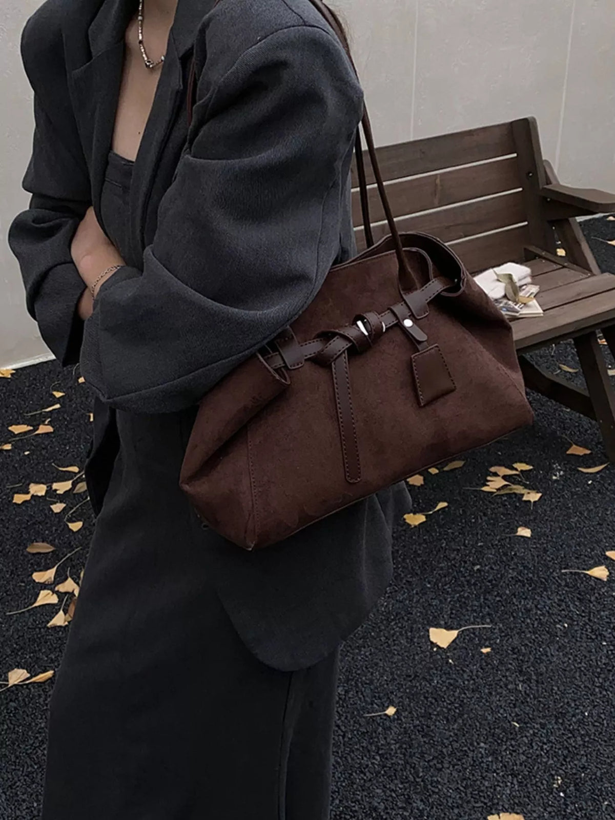 Brown suede shoulder bag with buckle straps and front charm tag, side view