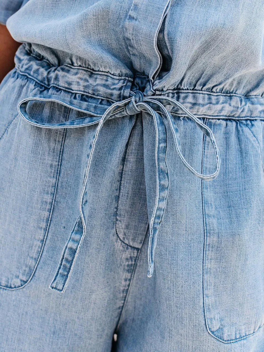 Light blue denim romper close-up: tie drawstring waist and side patch pockets