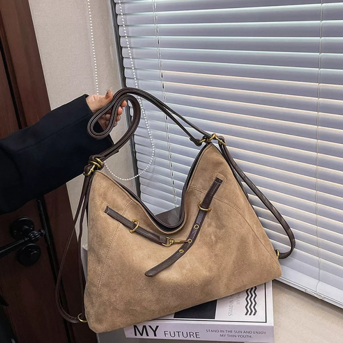 Tan suede shoulder bag with decorative buckle, wide straps and gold-tone hardware