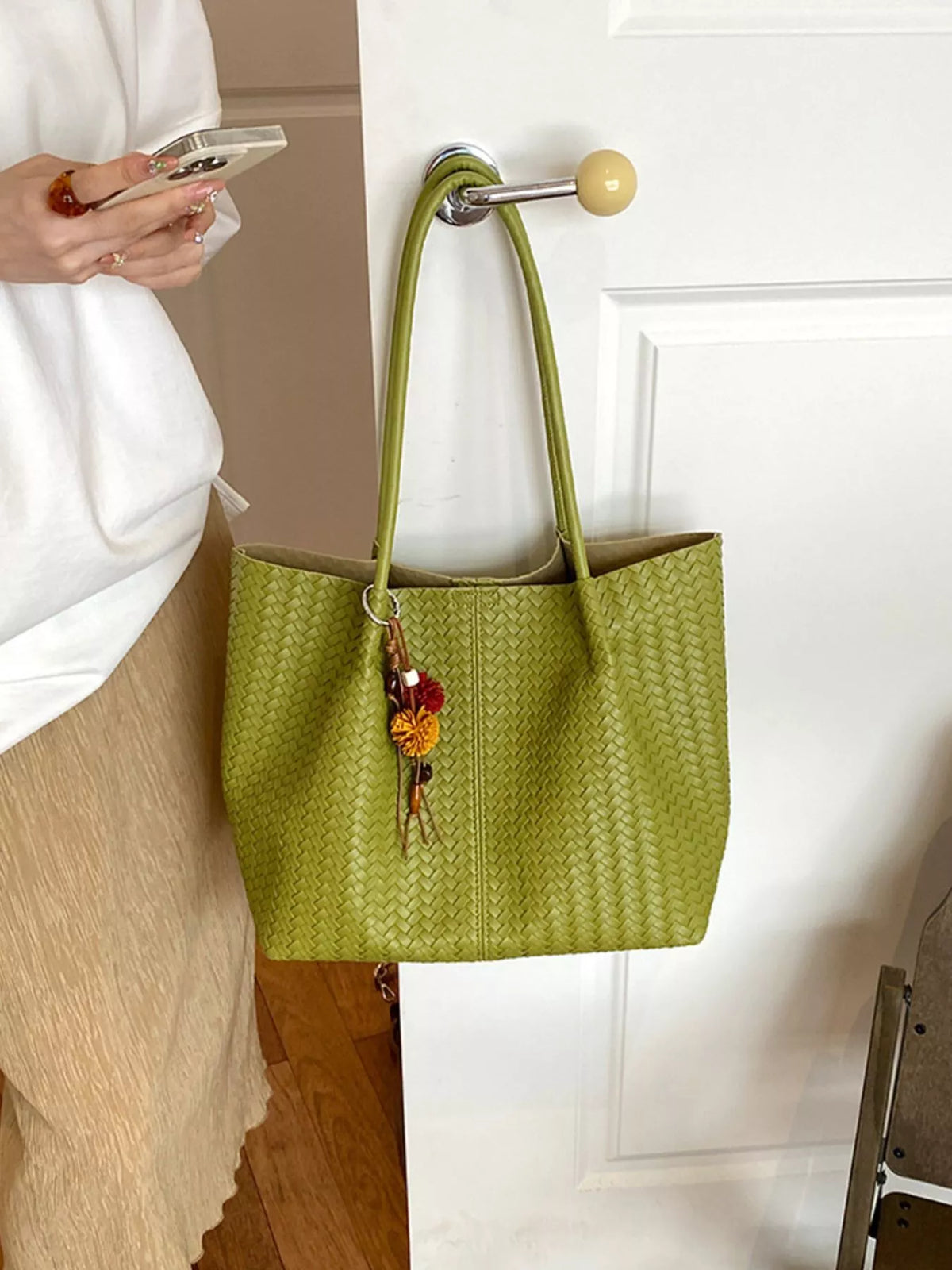 Green woven vegan leather tote bag with long handles and colorful tassel keychain charm