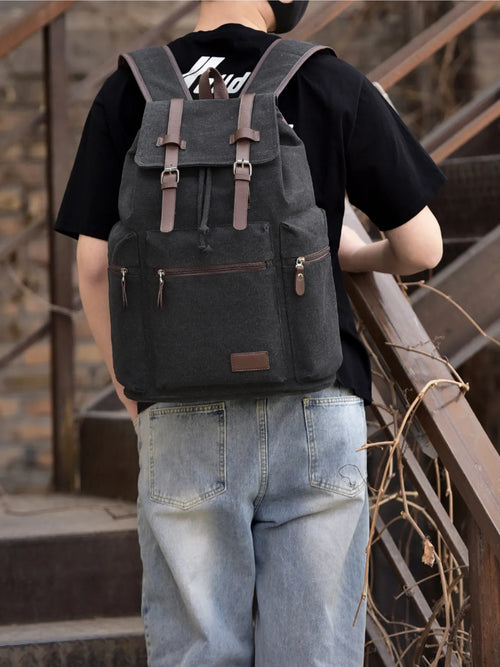 Black canvas backpack bag with front flap, buckle straps, and zip pocket
