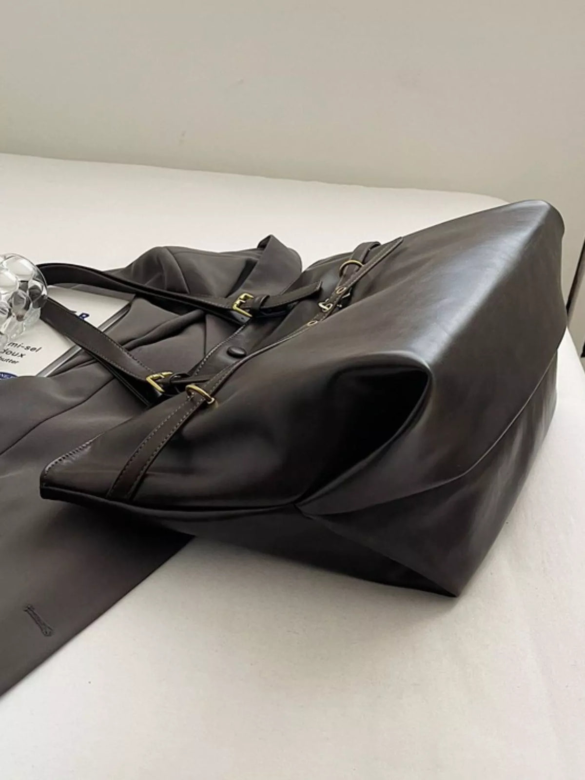 Large vegan leather tote bag, black, folded side view with shoulder strap and hardware