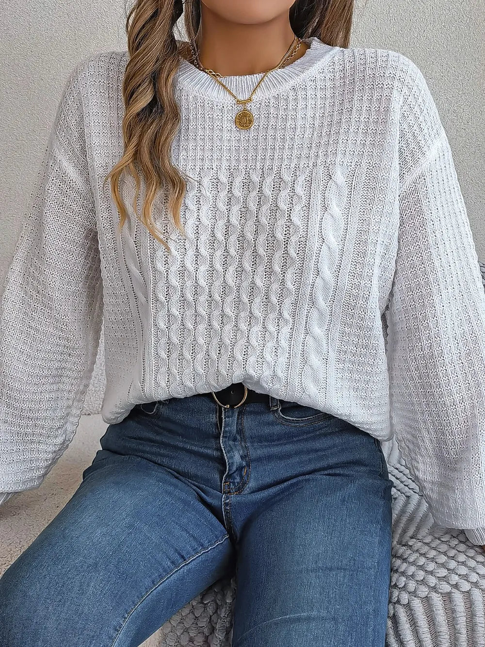 White cable-knit round-neck sweater with long sleeves and textured cable knit pattern.
