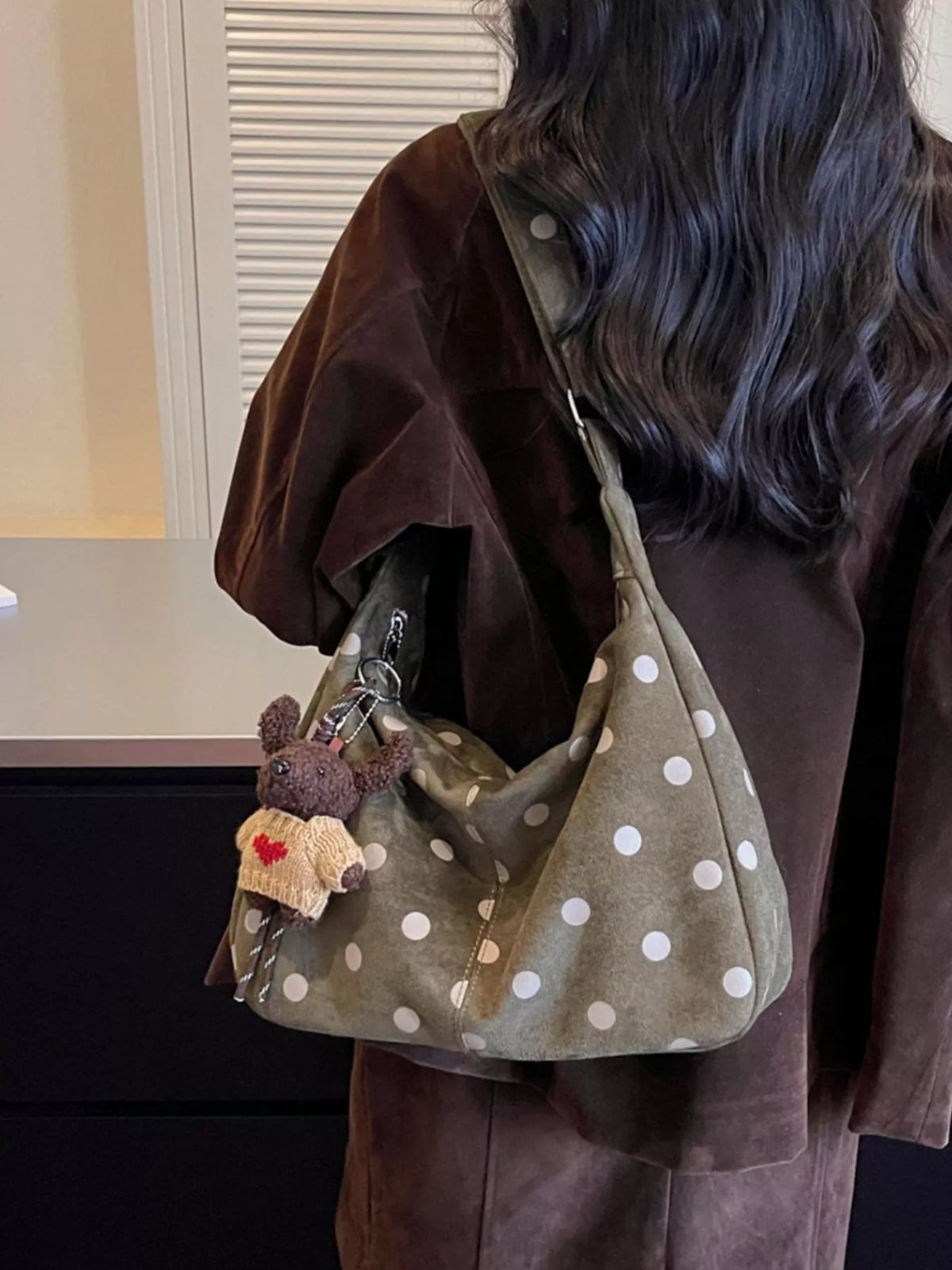 Green suede polka-dot shoulder bag worn crossbody with teddy keychain and side strap