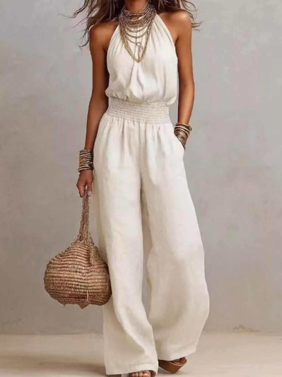 White smocked halter neck wide-leg jumpsuit with gathered waist and sleeveless bodice.