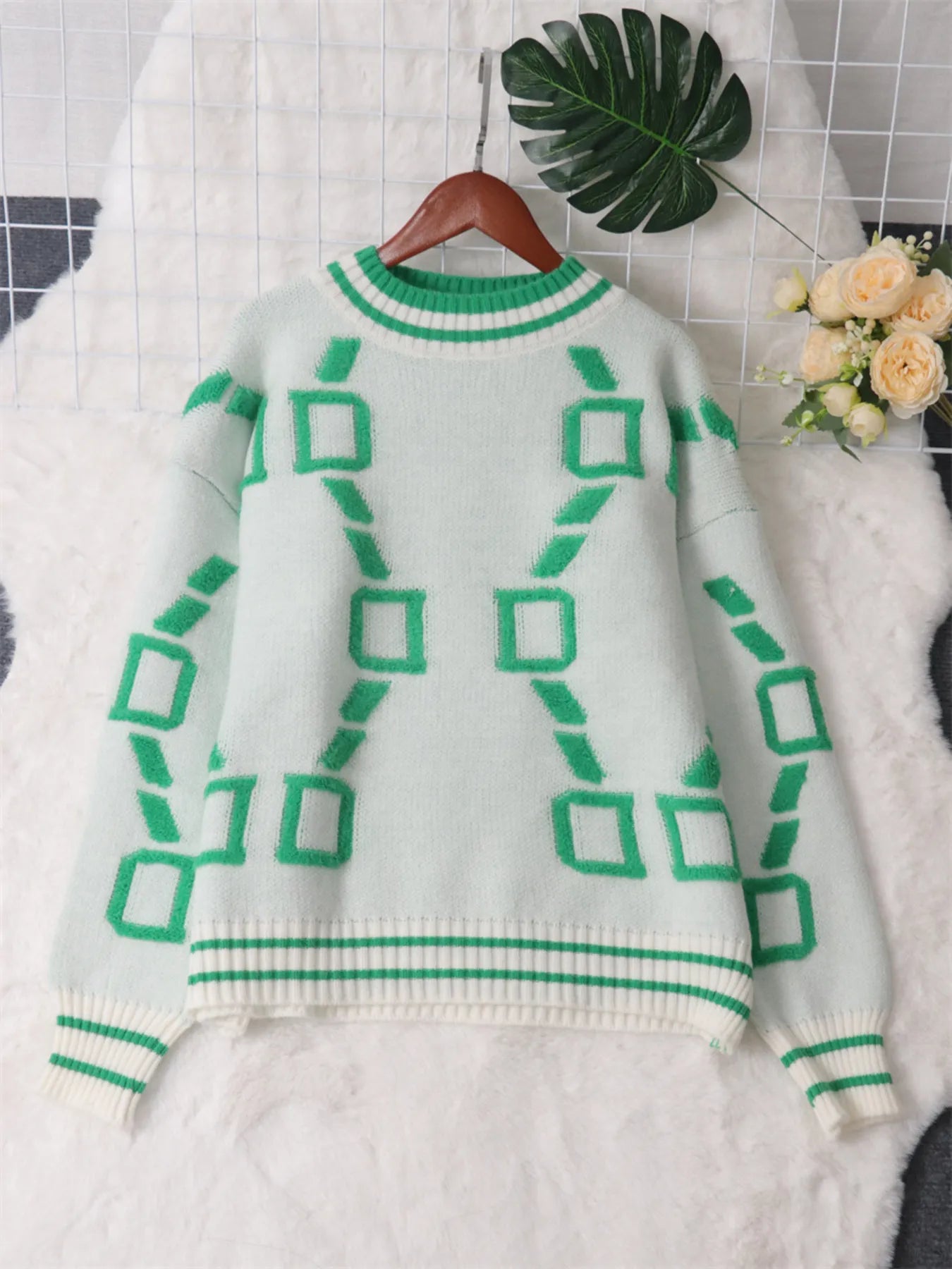 White round-neck long-sleeve sweater on hanger with green geometric motif