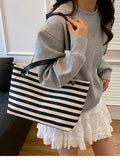 Black and white striped shoulder bag held by a person; gold chain handles and zip top.