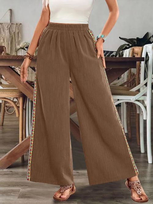Brown bohemian wide-leg pants with elastic waist and colorful embroidered side stripe.
