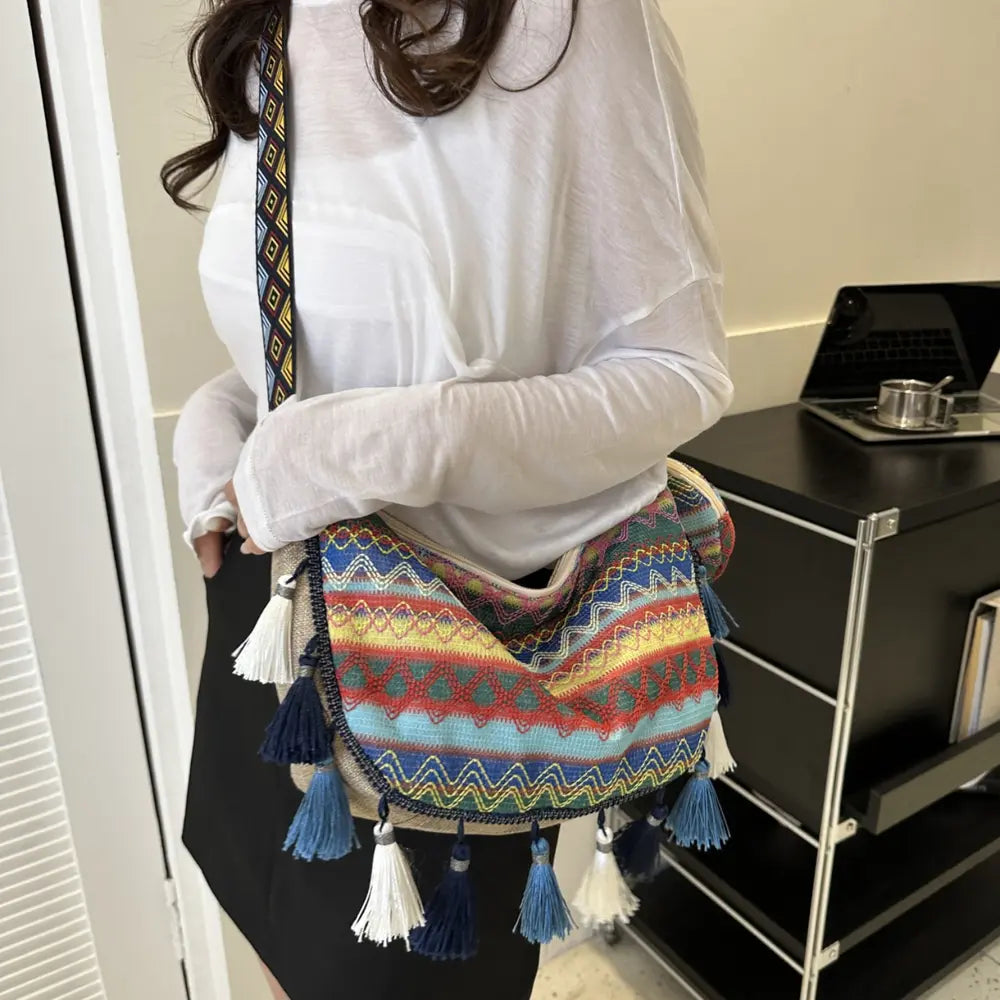 Printed crossbody bag on person with multicolor zigzag pattern and tassel fringe.