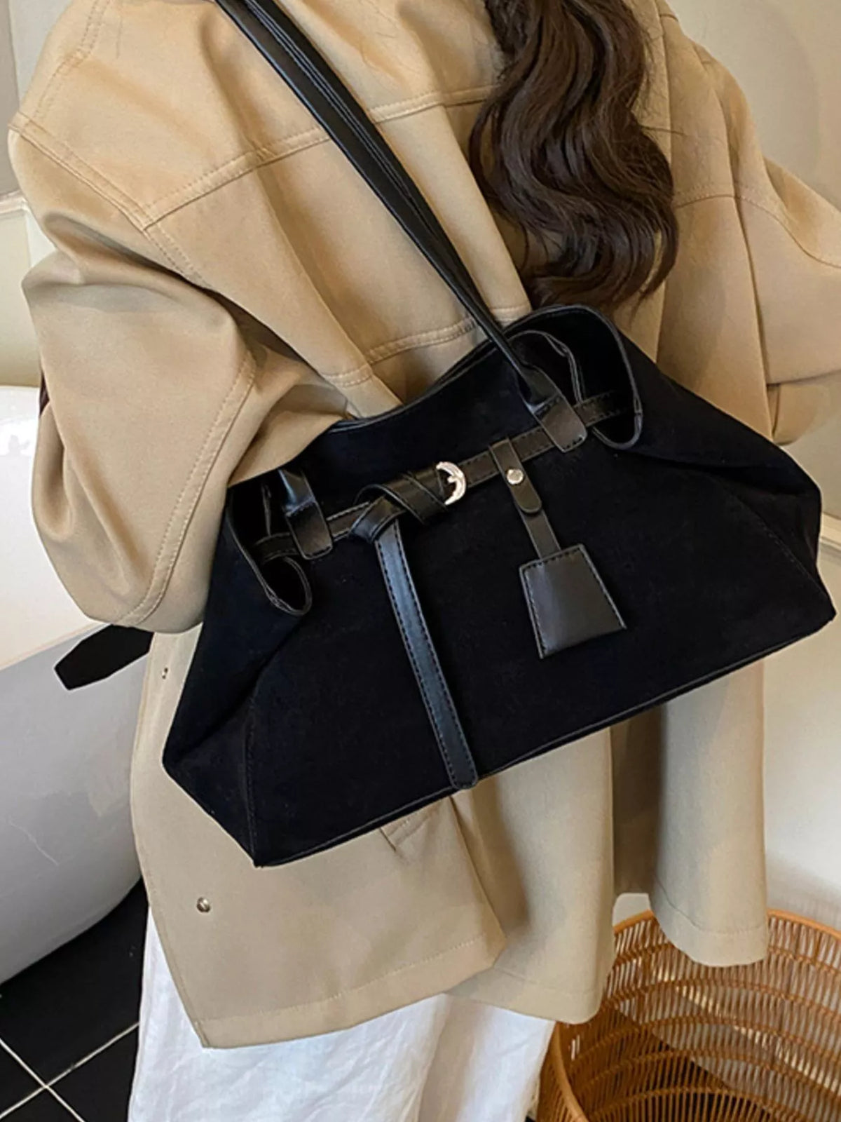Black suede shoulder bag with buckle strap and front hanging charm tag, angled view