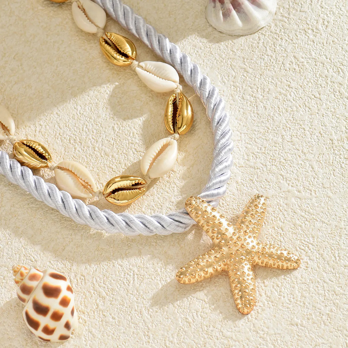 Rope necklace detail with gold starfish charm, white shell links, and braided rope
