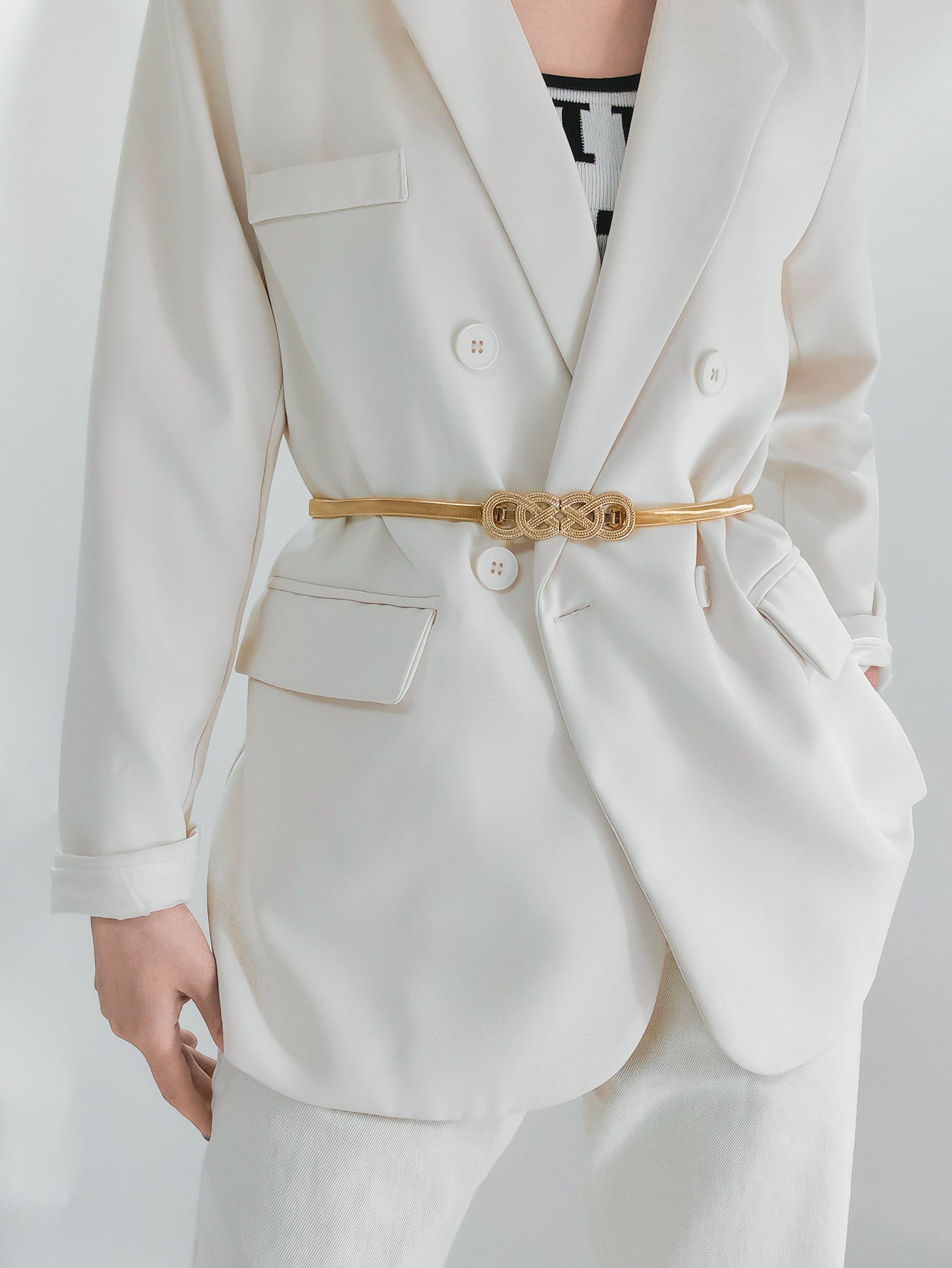 Gold-tone metal knot buckle belt with braided center on a light suit jacket