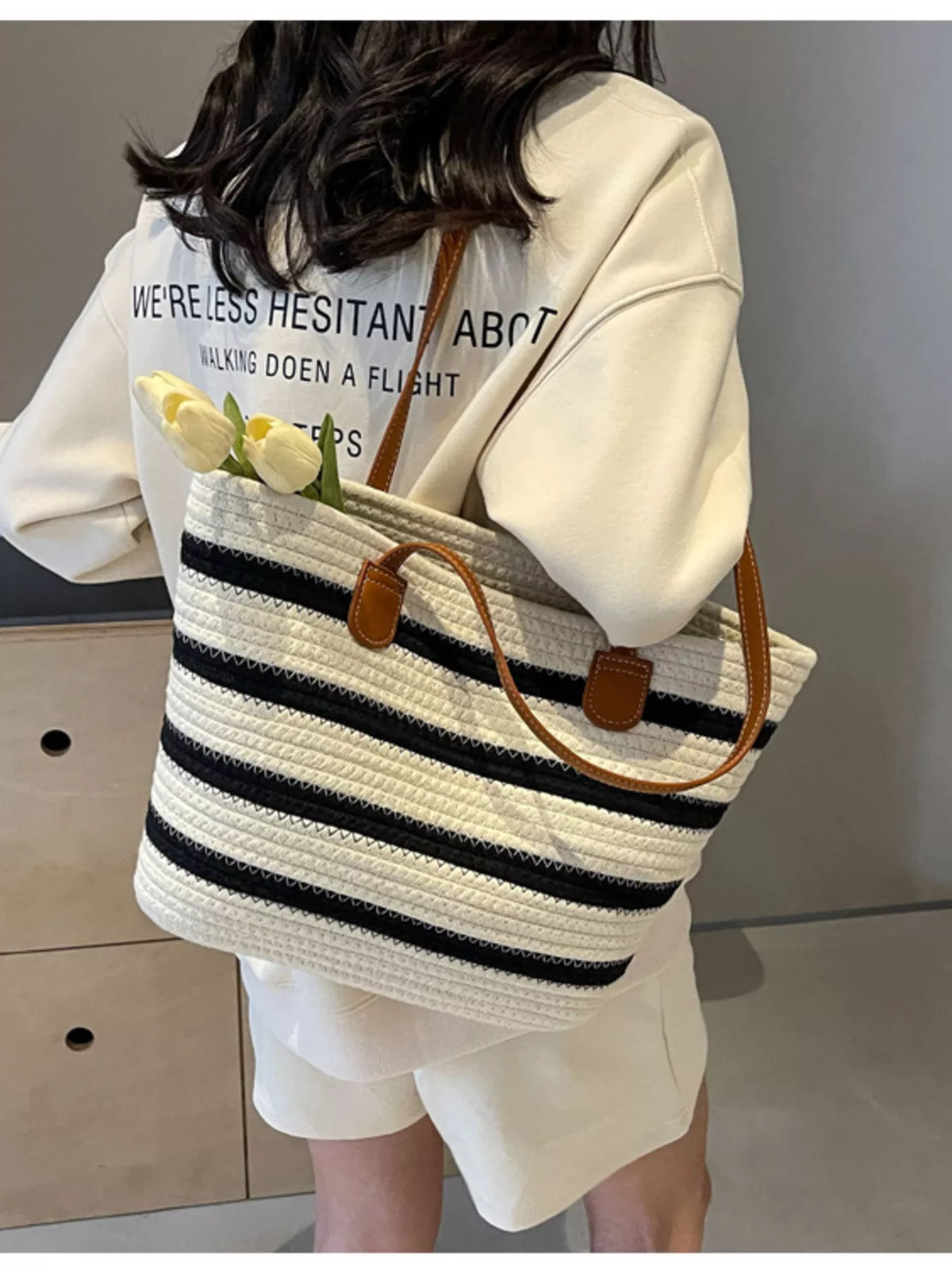 Striped straw tote bag featuring brown handle tabs and white weave with navy stripes