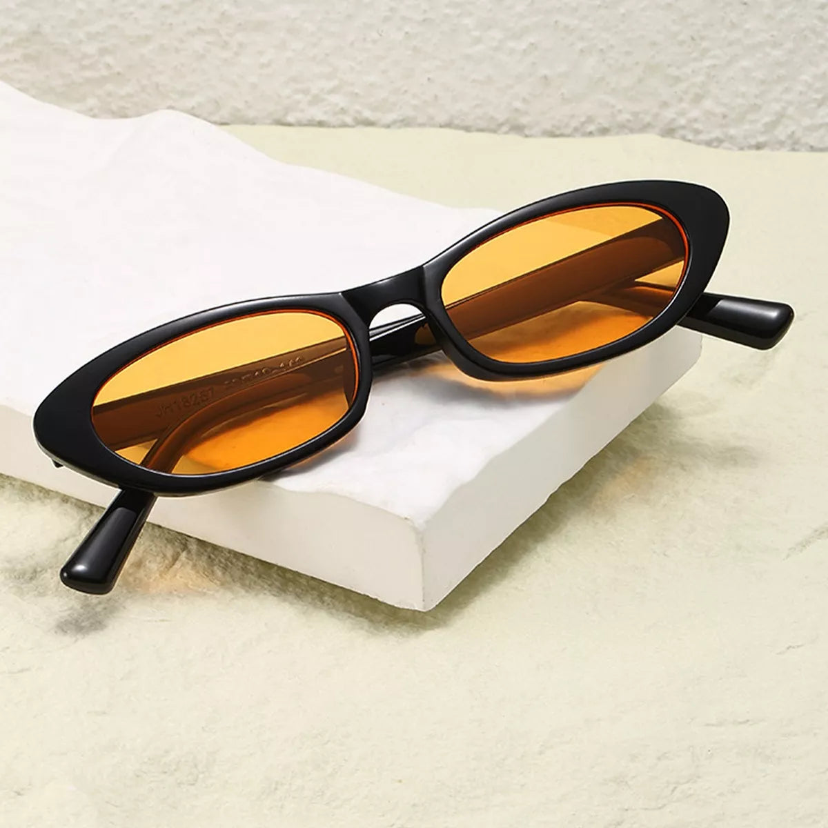 Black oval UV400 sunglasses with amber tinted lenses on a white box