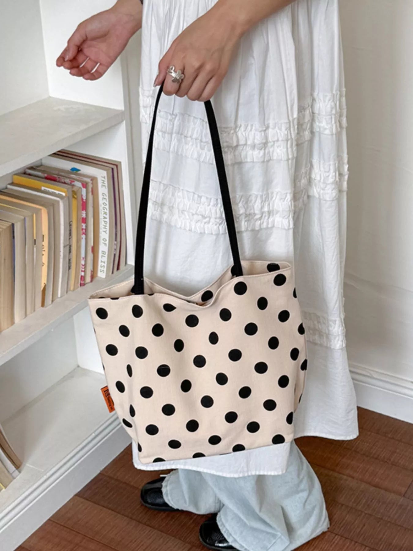 Cream polka dot shoulder tote with black dots and black handles, held at side