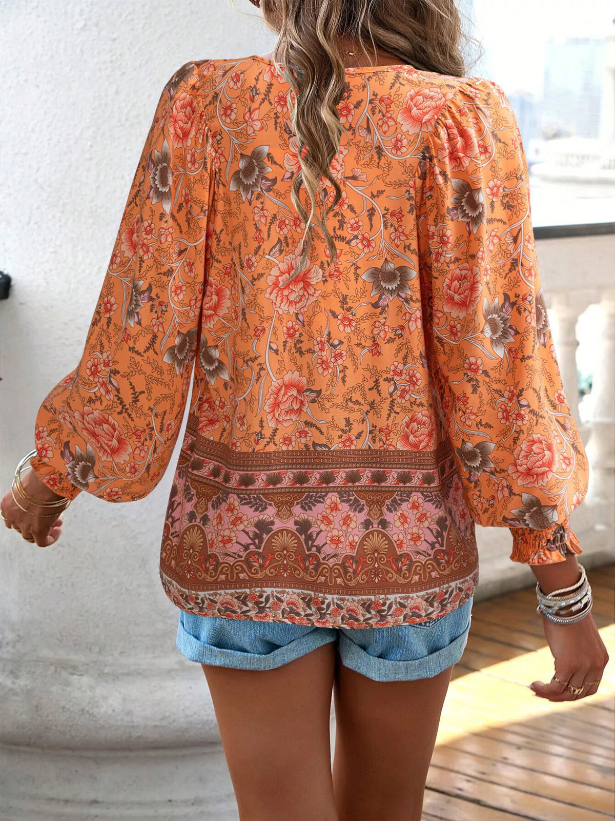 Back view of orange floral tie-neck blouse with smocked cuffs and border print