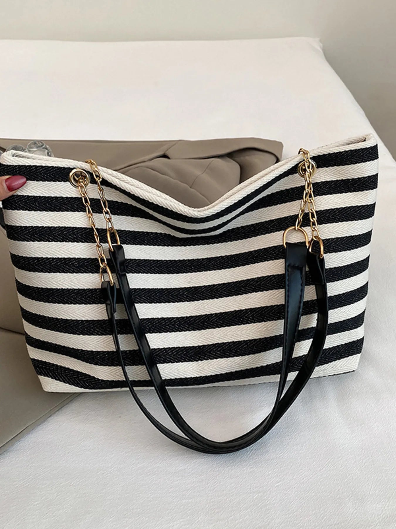 Striped shoulder bag with black-and-white canvas sides, gold chain handles, and zipper top.