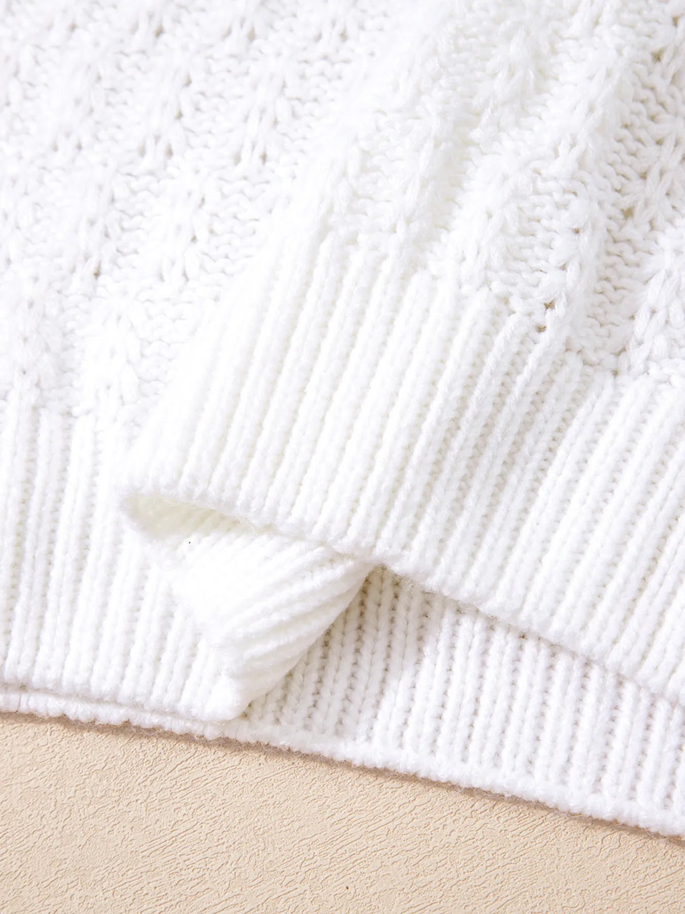 White ribbed knit sleeve cuff and textured body of loose V-neck sweater