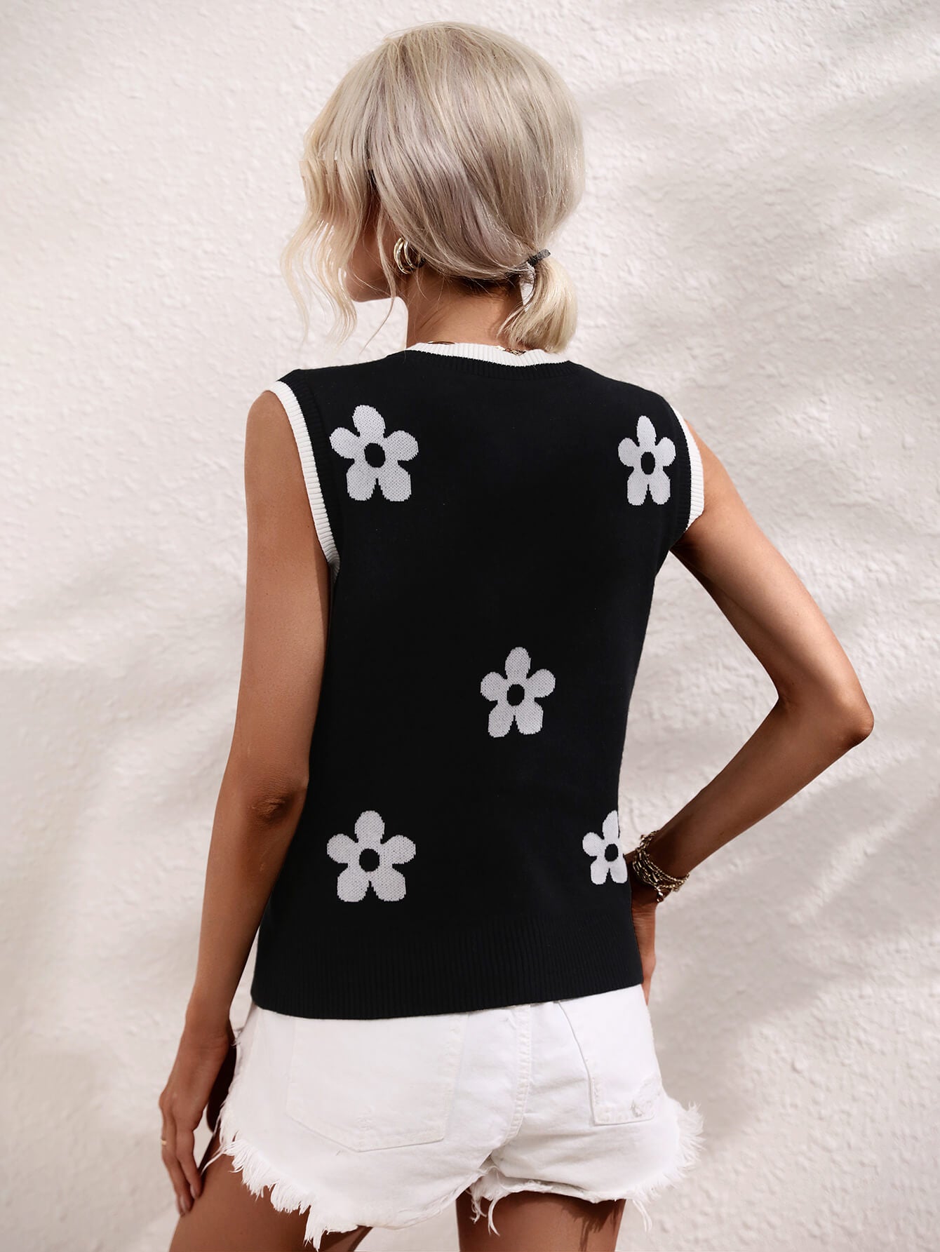 Black sleeveless sweater vest with V-neck back and white flower motifs, ribbed trim.