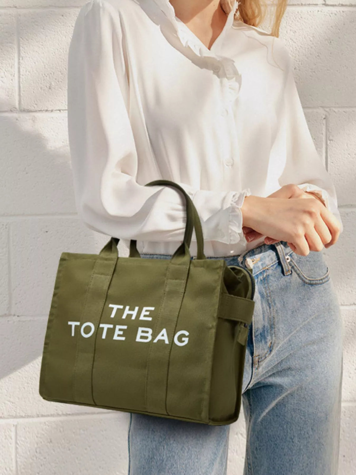 Army green canvas tote bag with “THE TOTE BAG” lettering, worn with knotted handles
