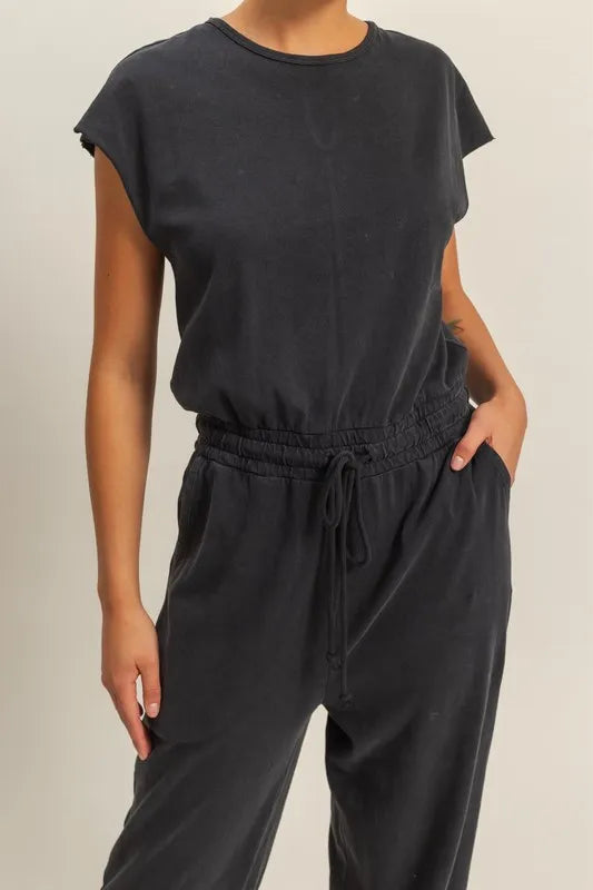 Black round-neck jumpsuit with cap sleeves and gathered drawstring waist, full-length.