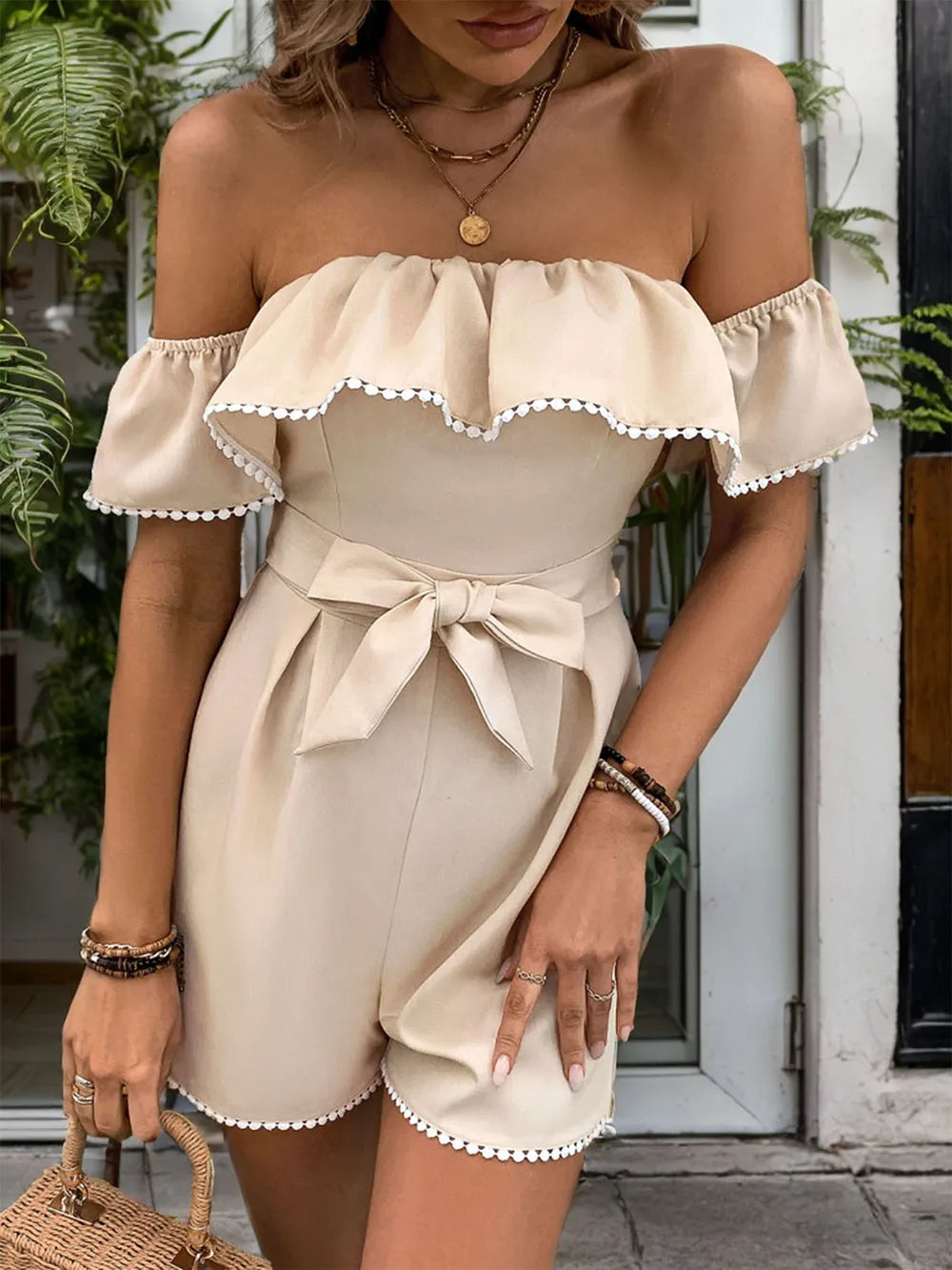 Light beige off-shoulder romper with ruffled neckline, waist bow, and scalloped shorts hem