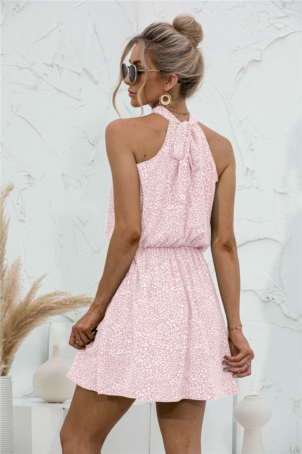 Back view of blush pink textured mini dress with halter tie and flared skirt