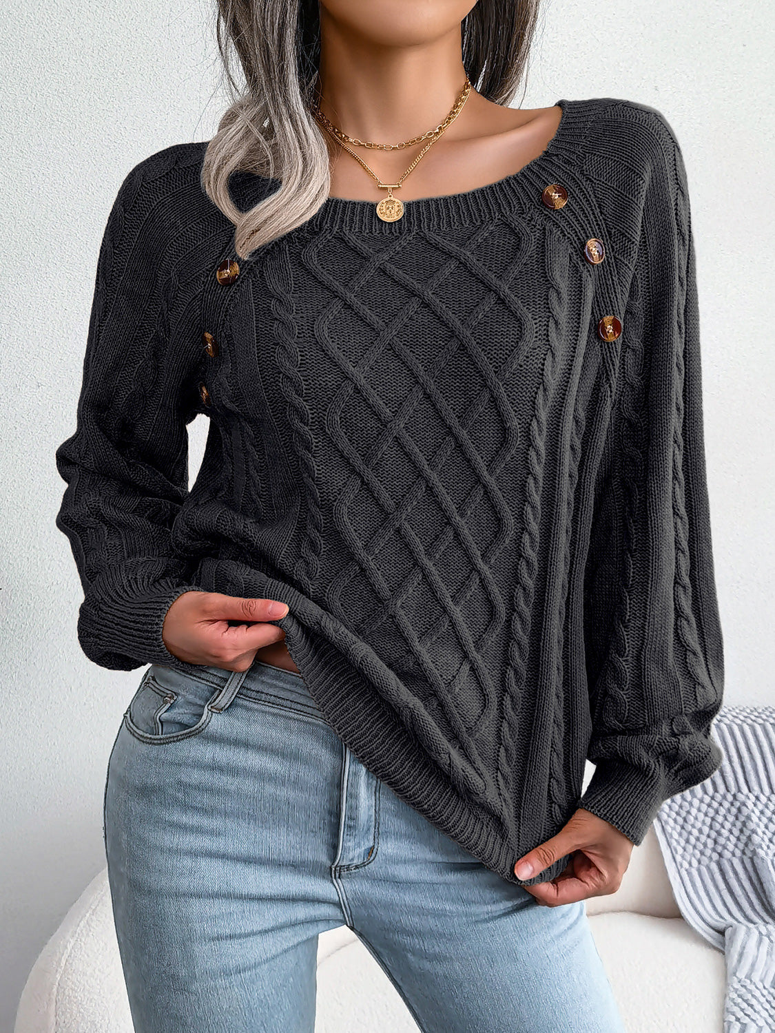 Black cable-knit sweater with diamond cable pattern and gold-tone decorative buttons