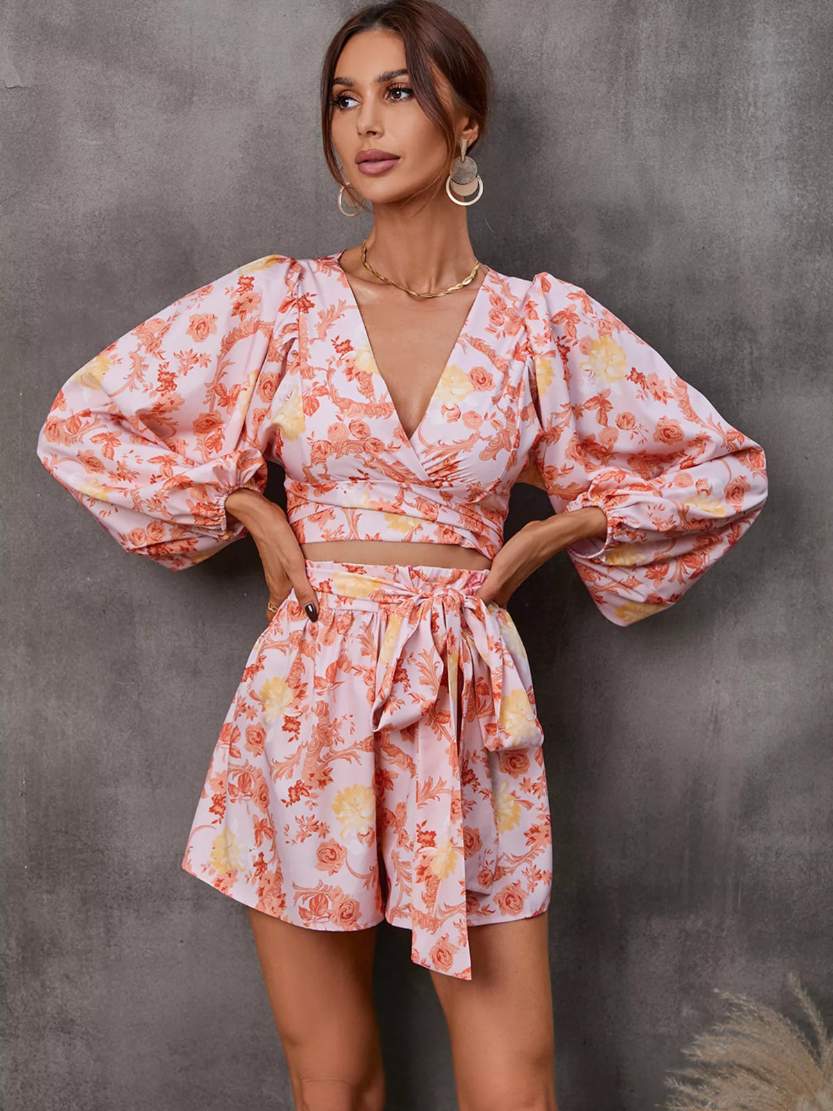 Printed long-sleeve romper with V-neck cutout and ruched waist; peach-orange floral print