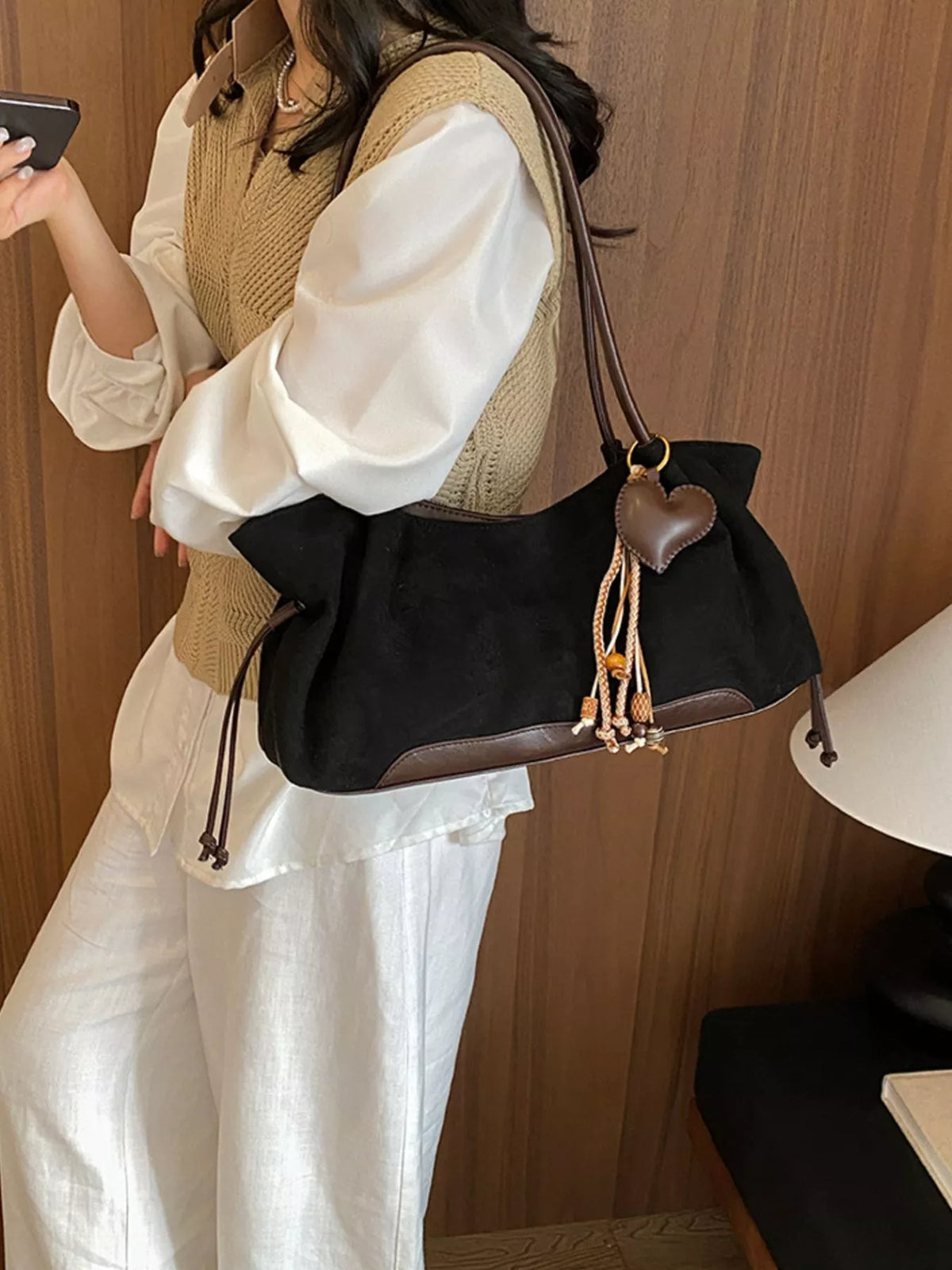Black suede drawstring shoulder bag with brown trim and hanging tassel pull cords