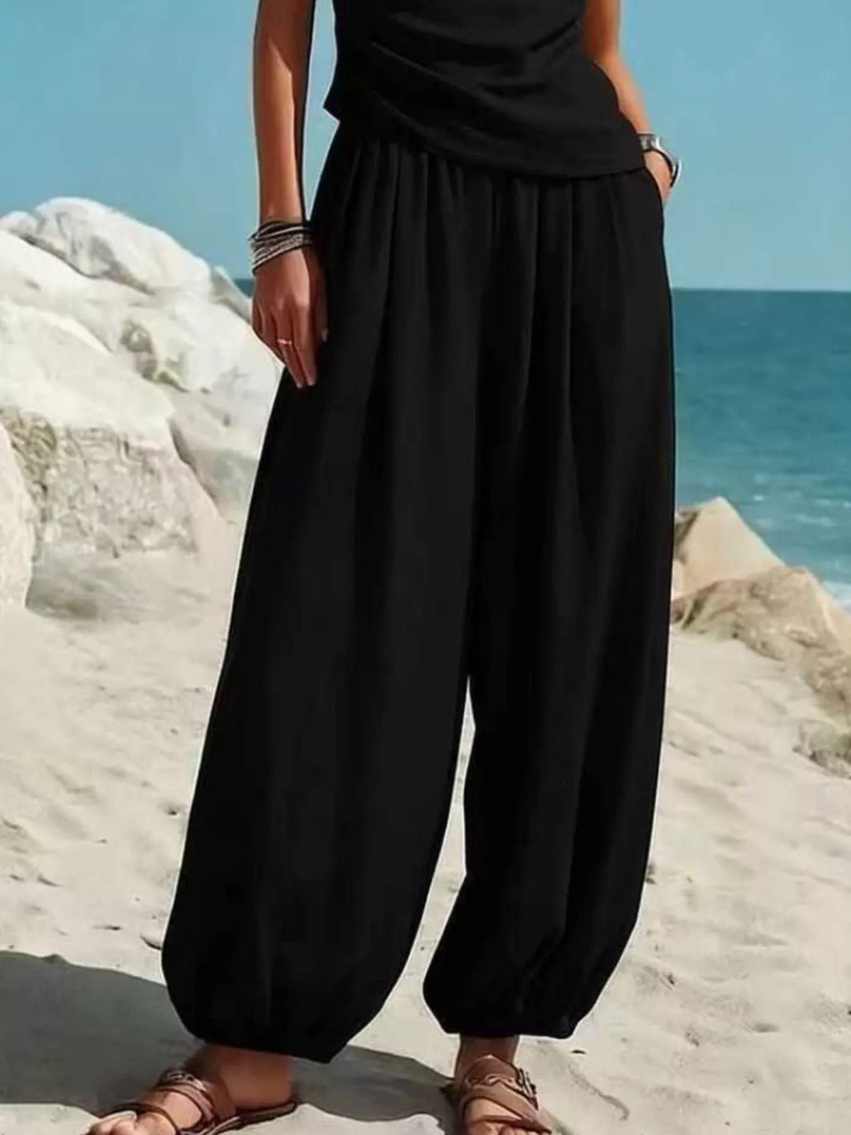 Black harem pants with gathered waistband and relaxed wide legs, paired with one-shoulder top