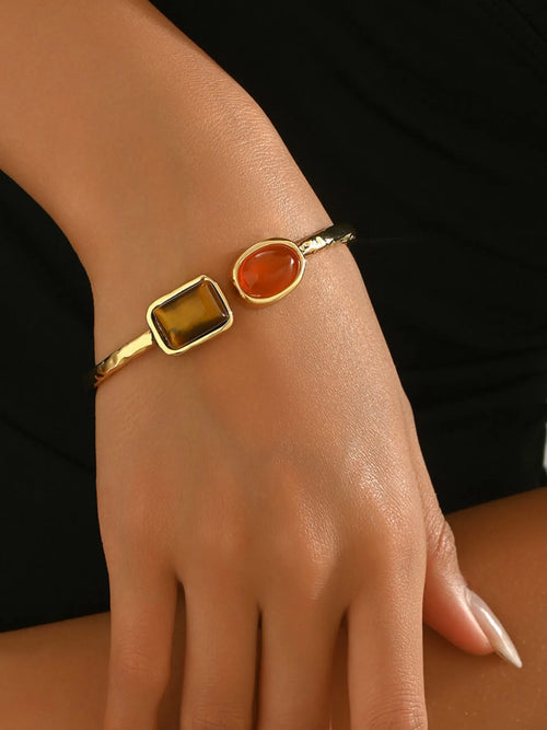 Gold tone geometric open bracelet on wrist with orange oval and dark square insets