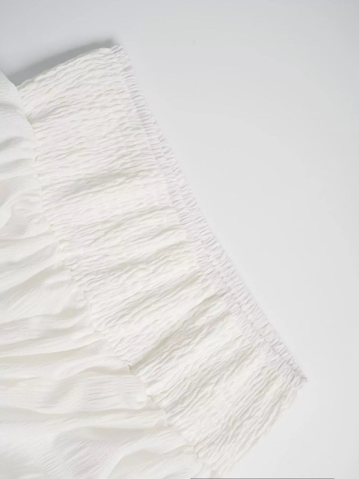 White fabric close-up showing smocked waistband and gathered tier seams
