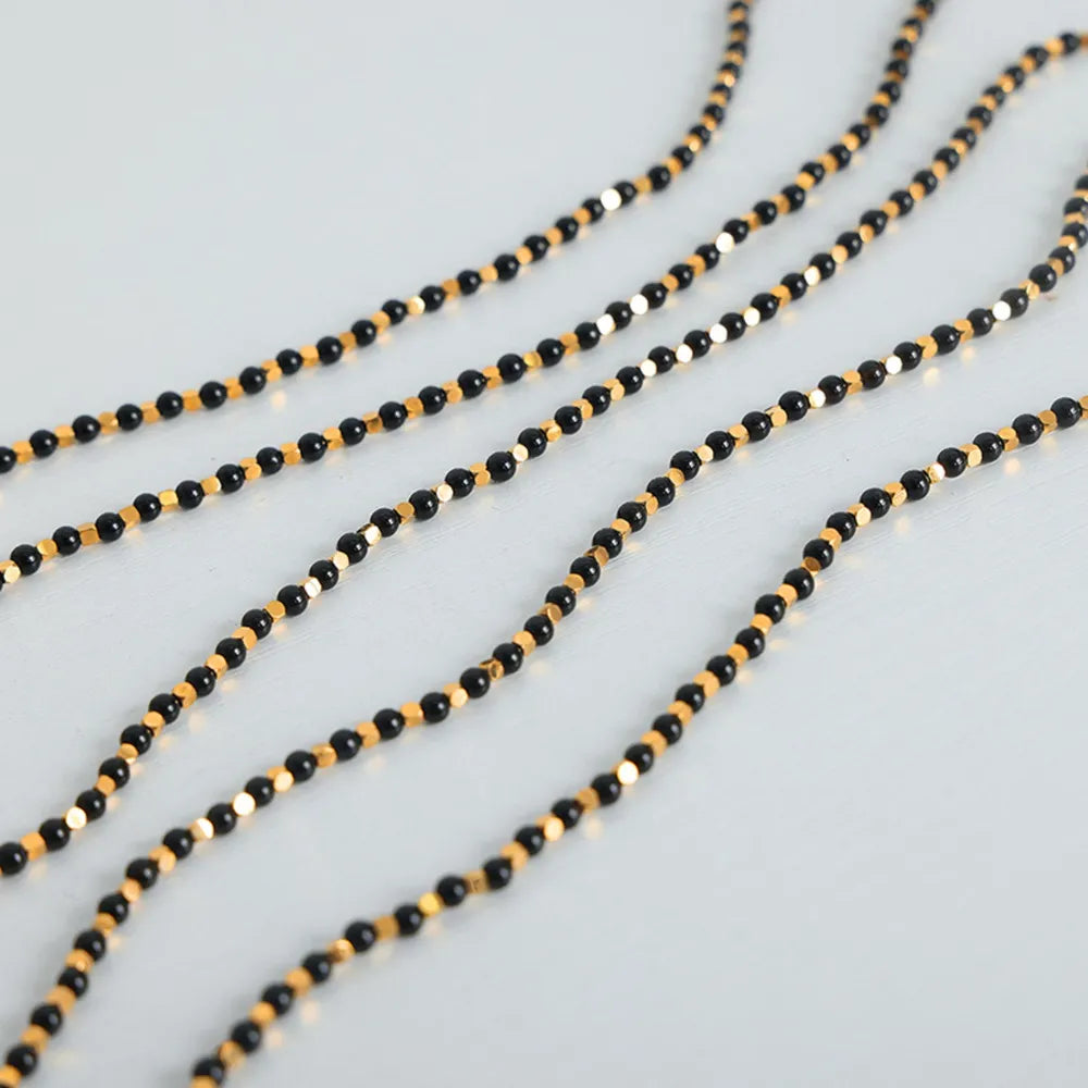 Agate beaded necklace with black beads and gold-tone highlights on white surface