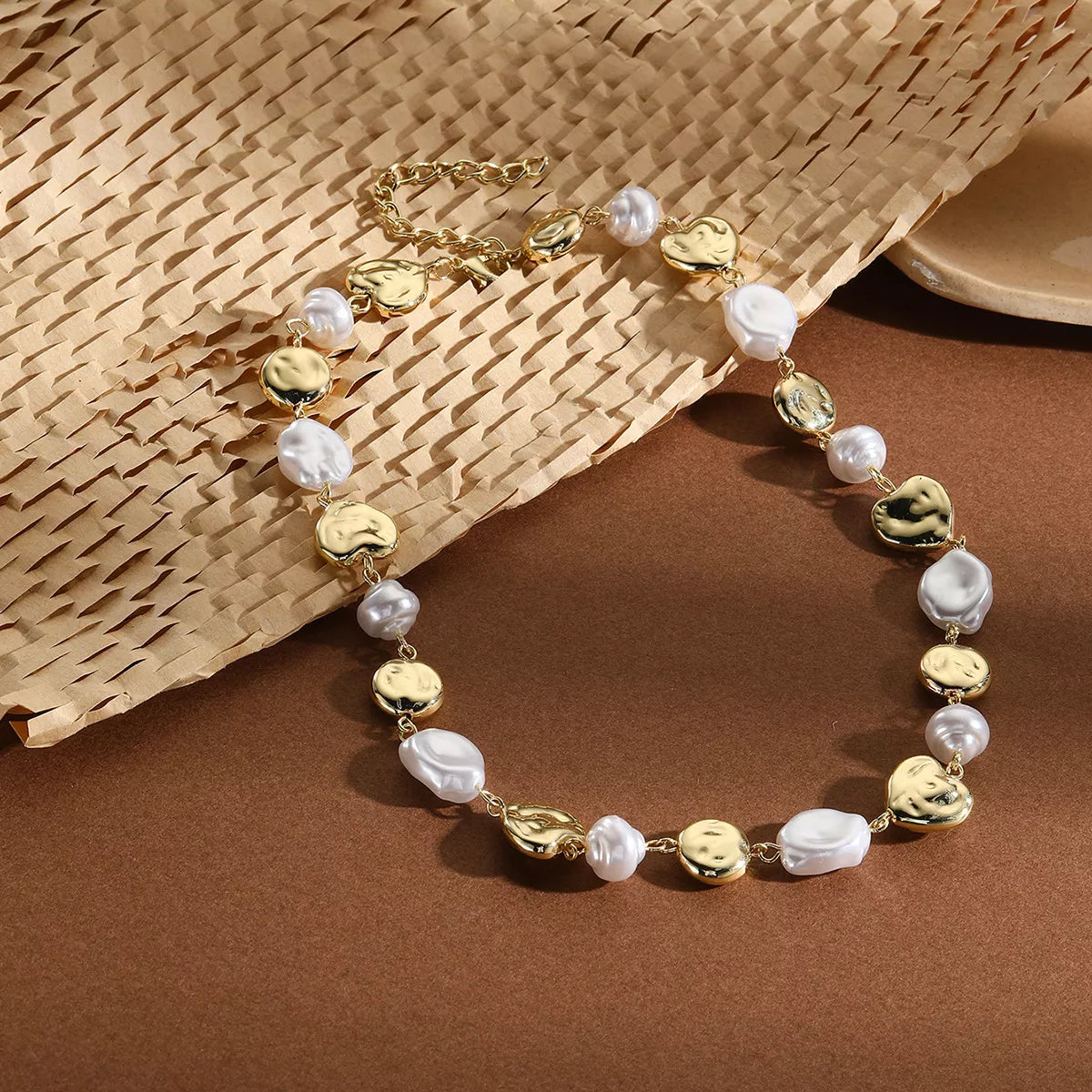 Pearl chain necklace with gold-tone coin beads and white pearl drops, flat lay