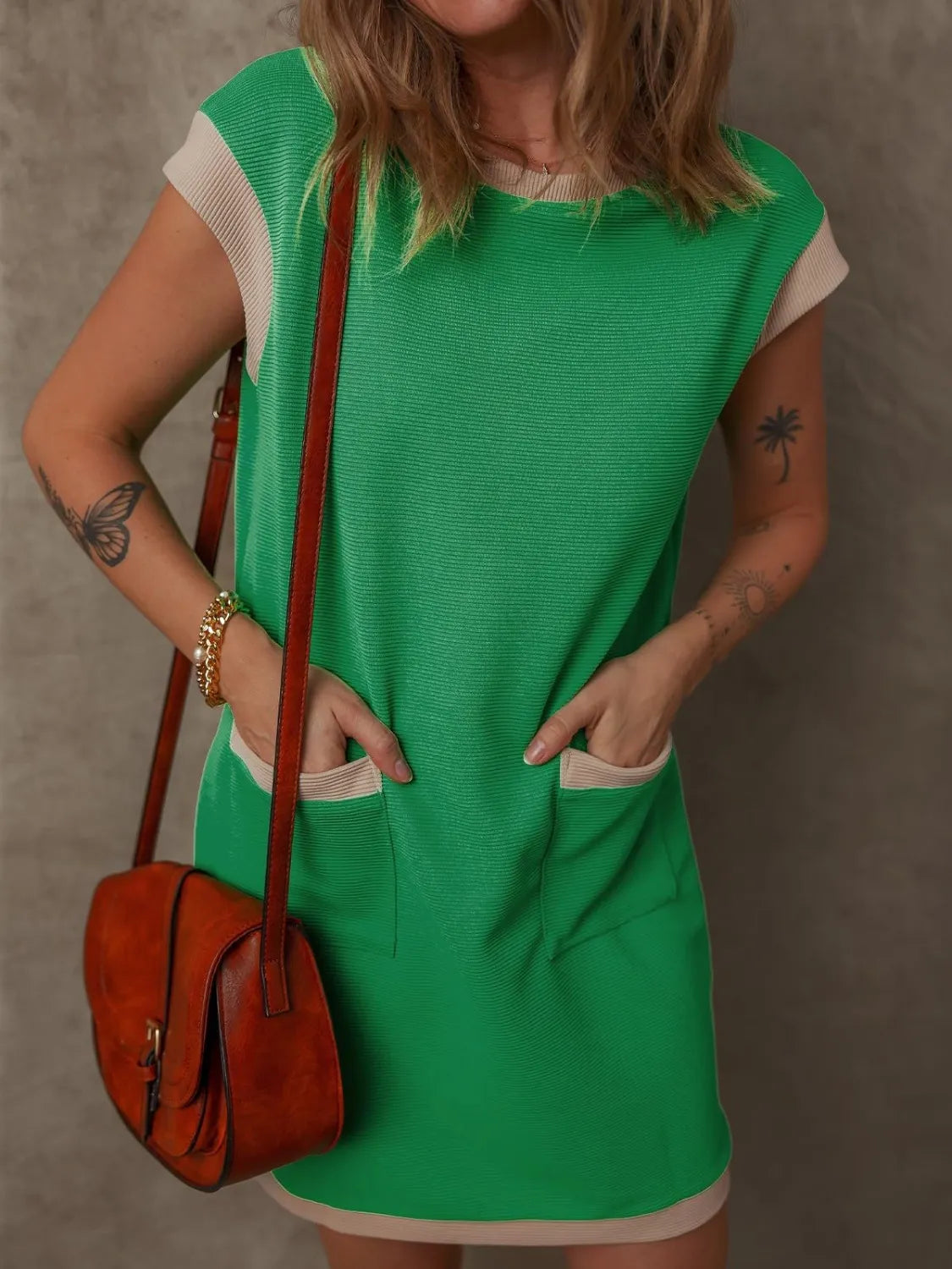 Round-neck cap-sleeve mini dress in green with beige-trim pockets, paired with a brown crossbody bag