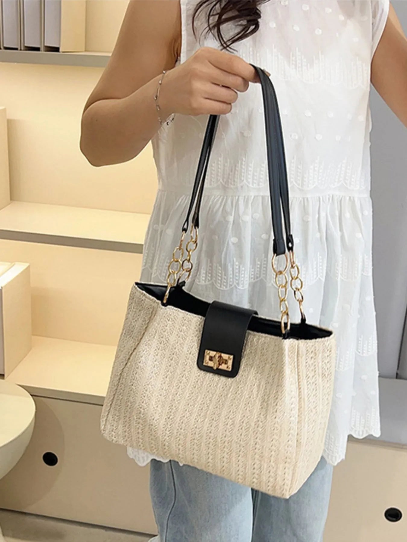 Beige woven straw shoulder bag with black top handles, gold chain, and front flap clasp