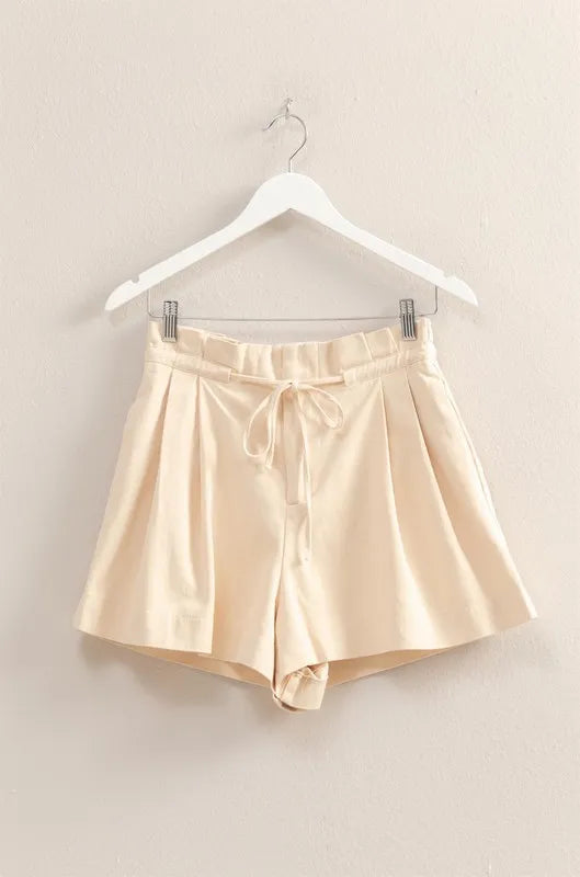 Oatmeal paperbag shorts laid flat on hanger, with drawstring waist and pleated front