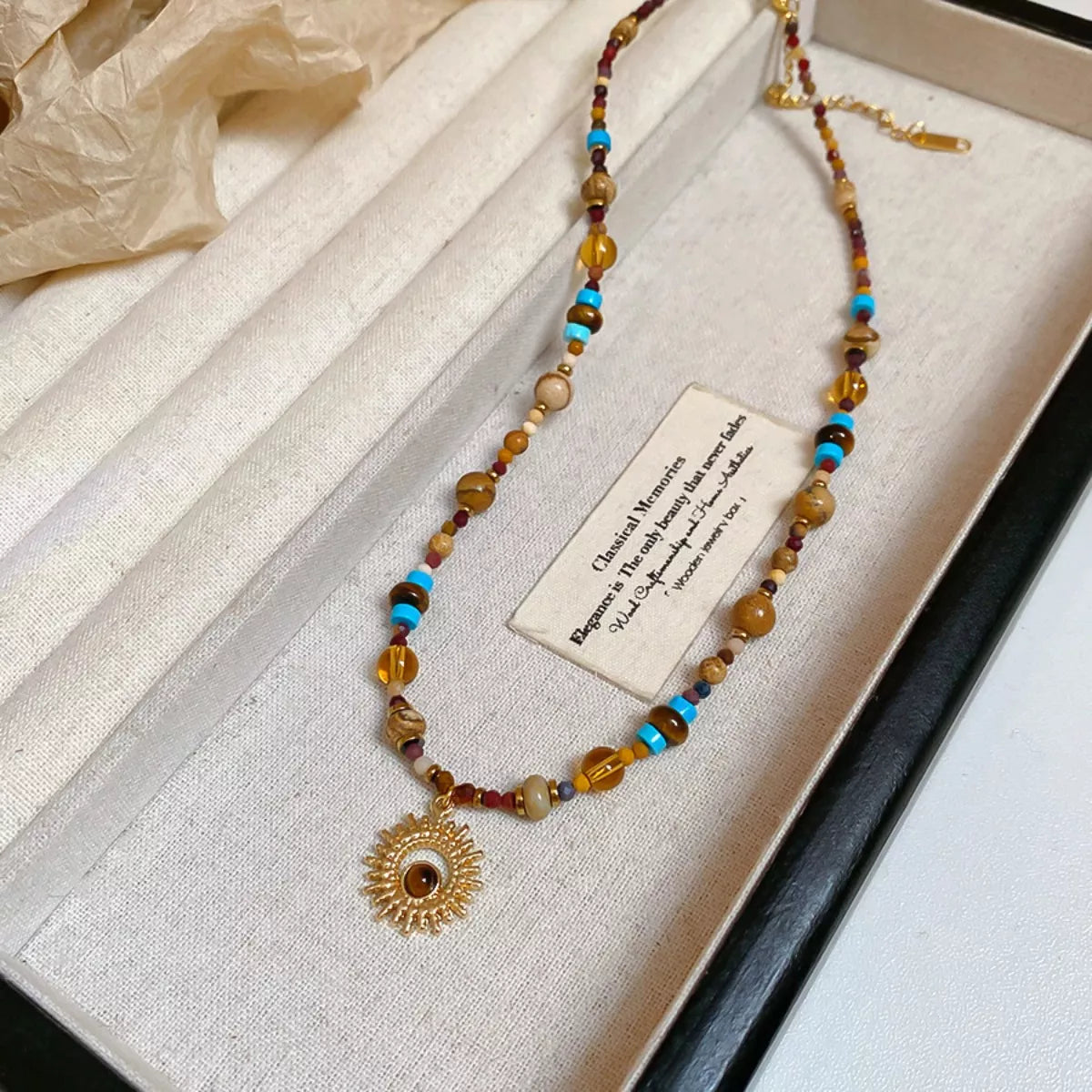 Gold-tone beaded sunflower pendant necklace on jewelry tray, multicolor beads