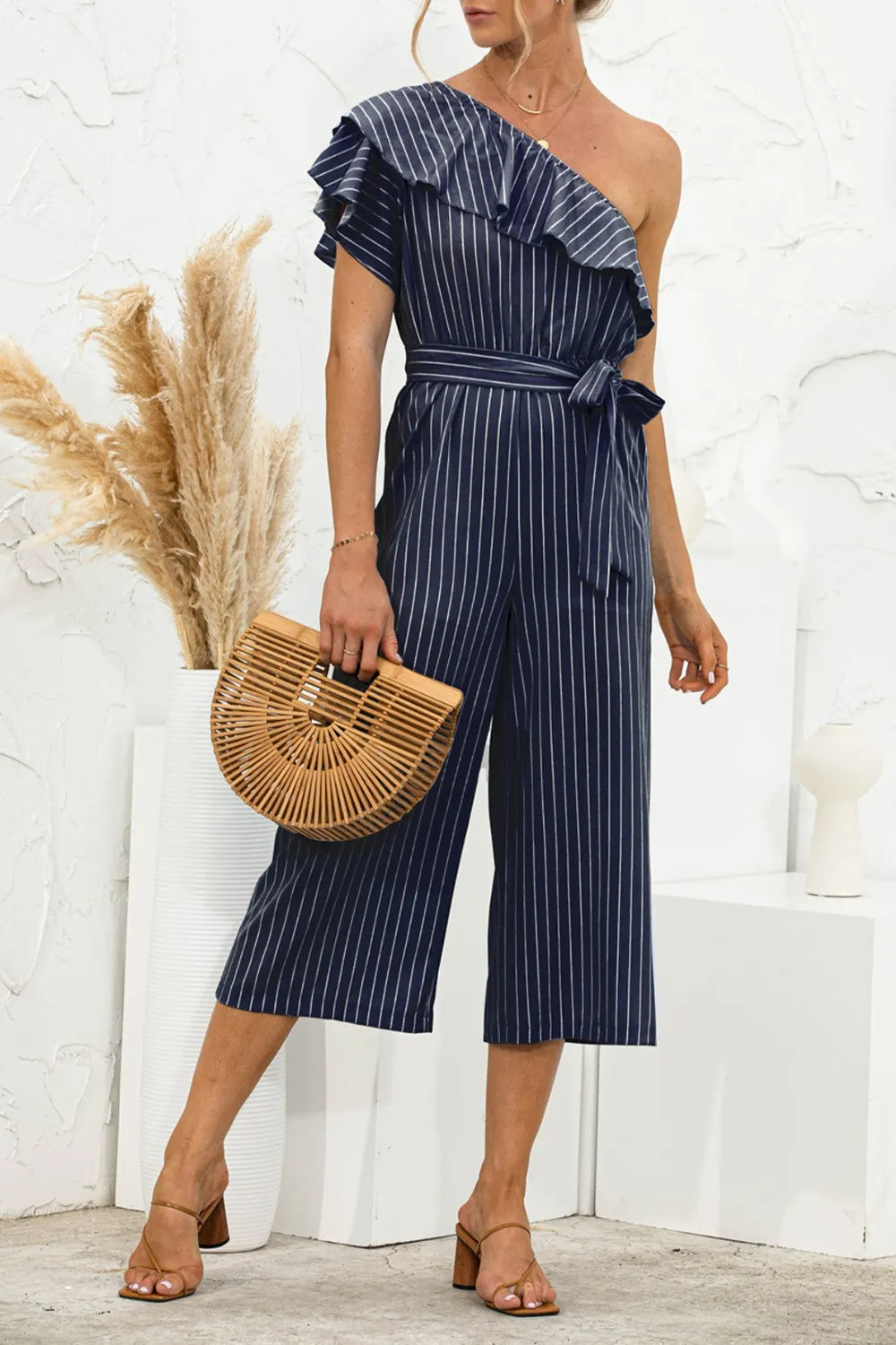 Dark blue pinstripe one-shoulder ruffle jumpsuit with waist tie and wide legs