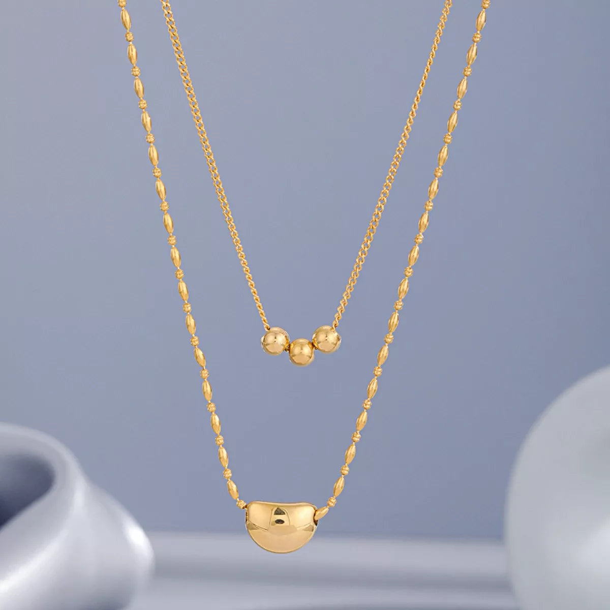 Gold double-layer necklace with triple-bead center and heart pendant on a longer chain.