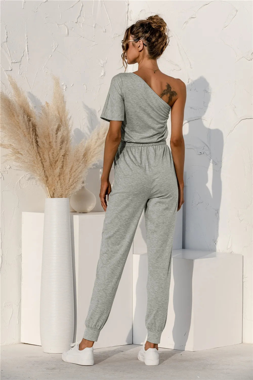 Gray one-shoulder short-sleeve jumpsuit with draped neckline, drawstring waist, tapered legs
