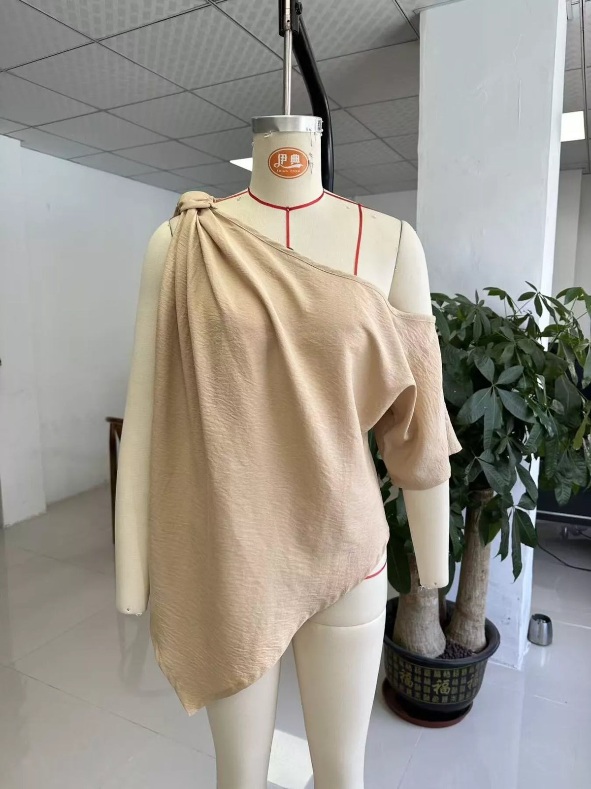 Khaki draped one-shoulder blouse with knotted neckline on a mannequin
