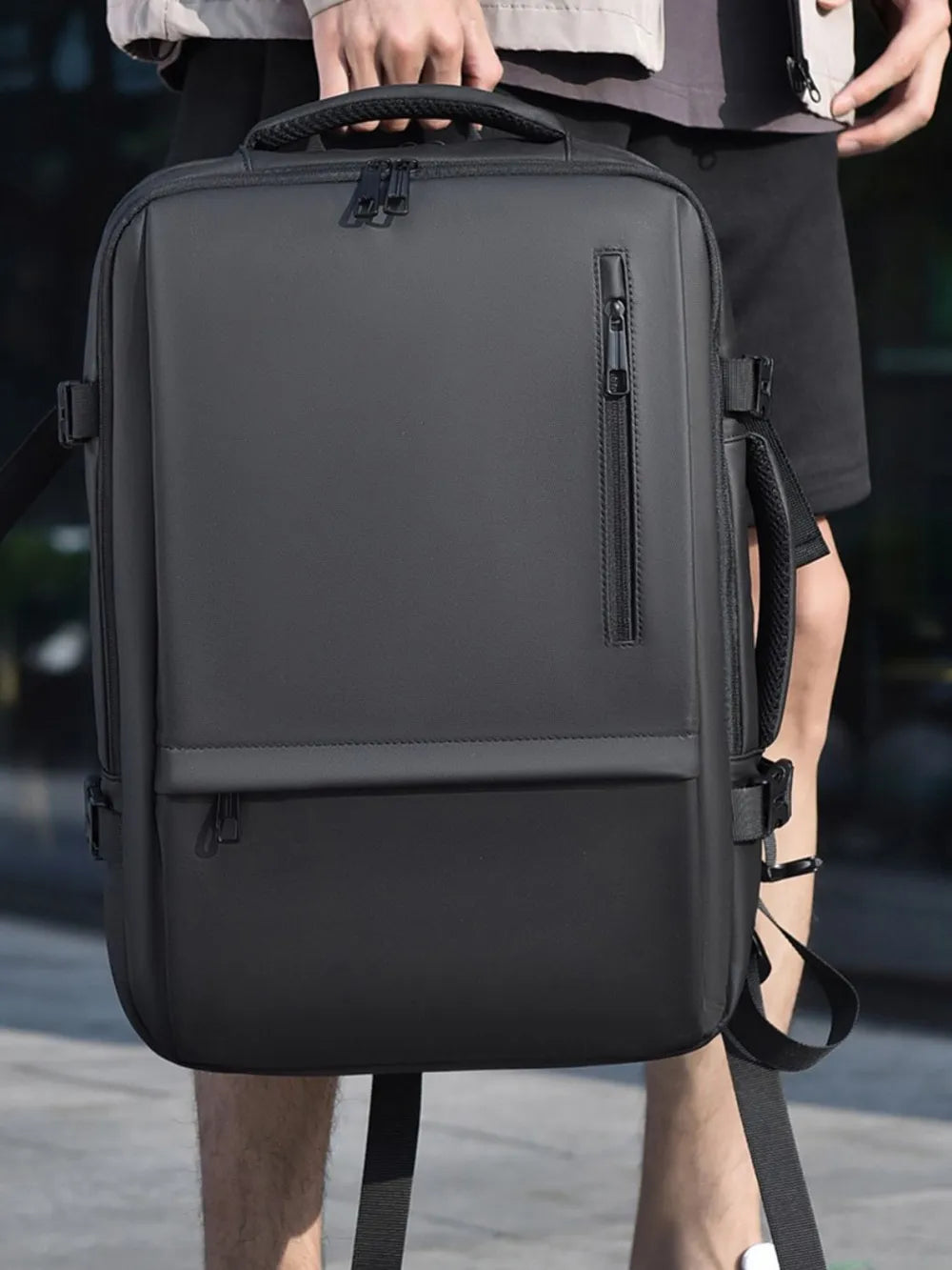 Black backpack worn on shoulder, with front zipper pocket and side compression straps.
