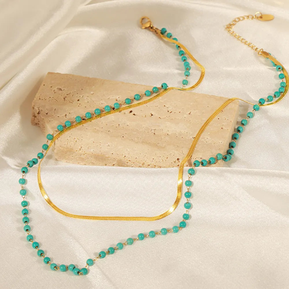 Turquoise bead double-layer necklace with gold links, laid on white fabric